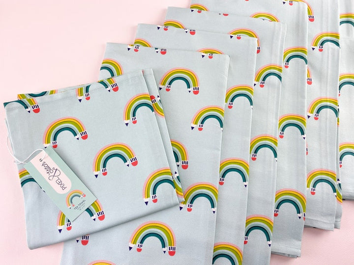 Set of colorful rainbow-patterned kitchen towels with pencils  arced to appear as a rainbow on a light blue background.