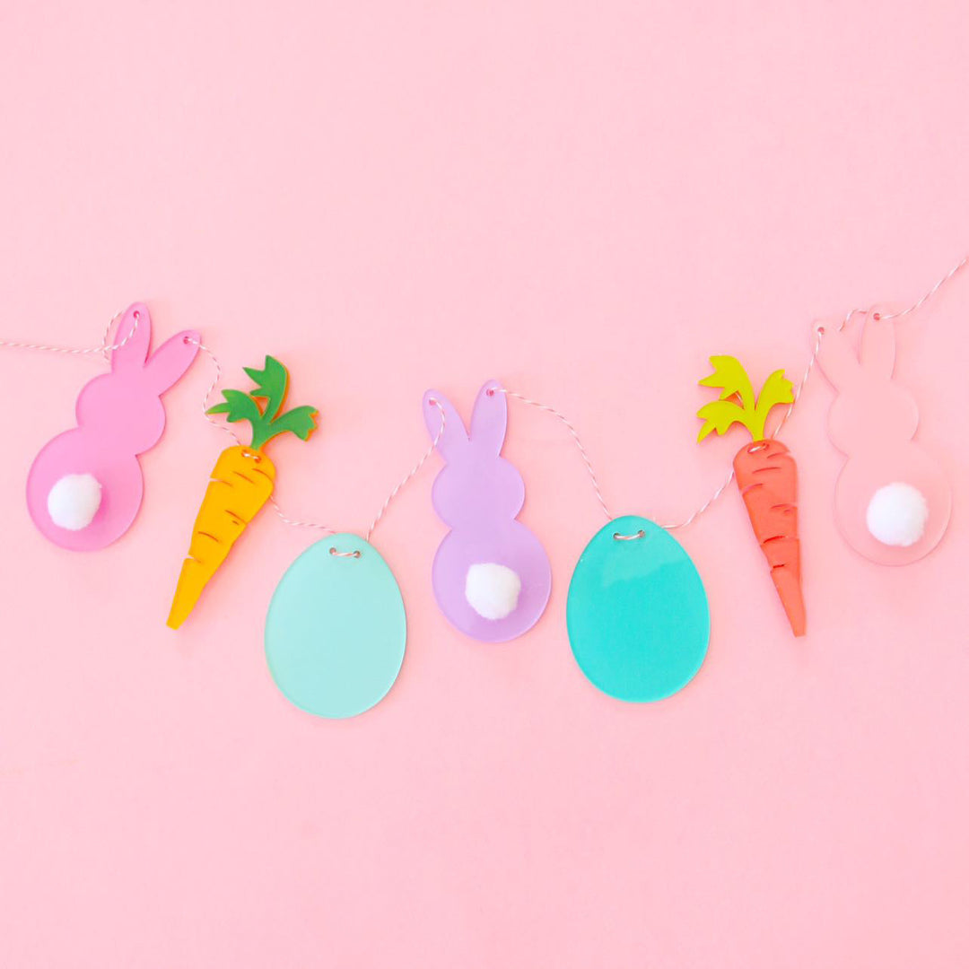 A string of 3 rabbits with white cottonball tails, 2 carrots and 2 eggs in pastel colors.