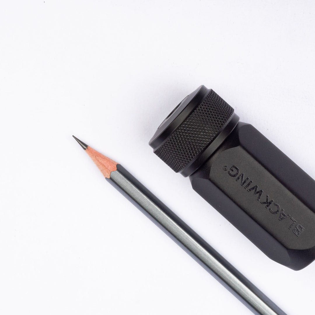 A black sharpener with a textured top and faceted sides next to a sharp gray pencil.