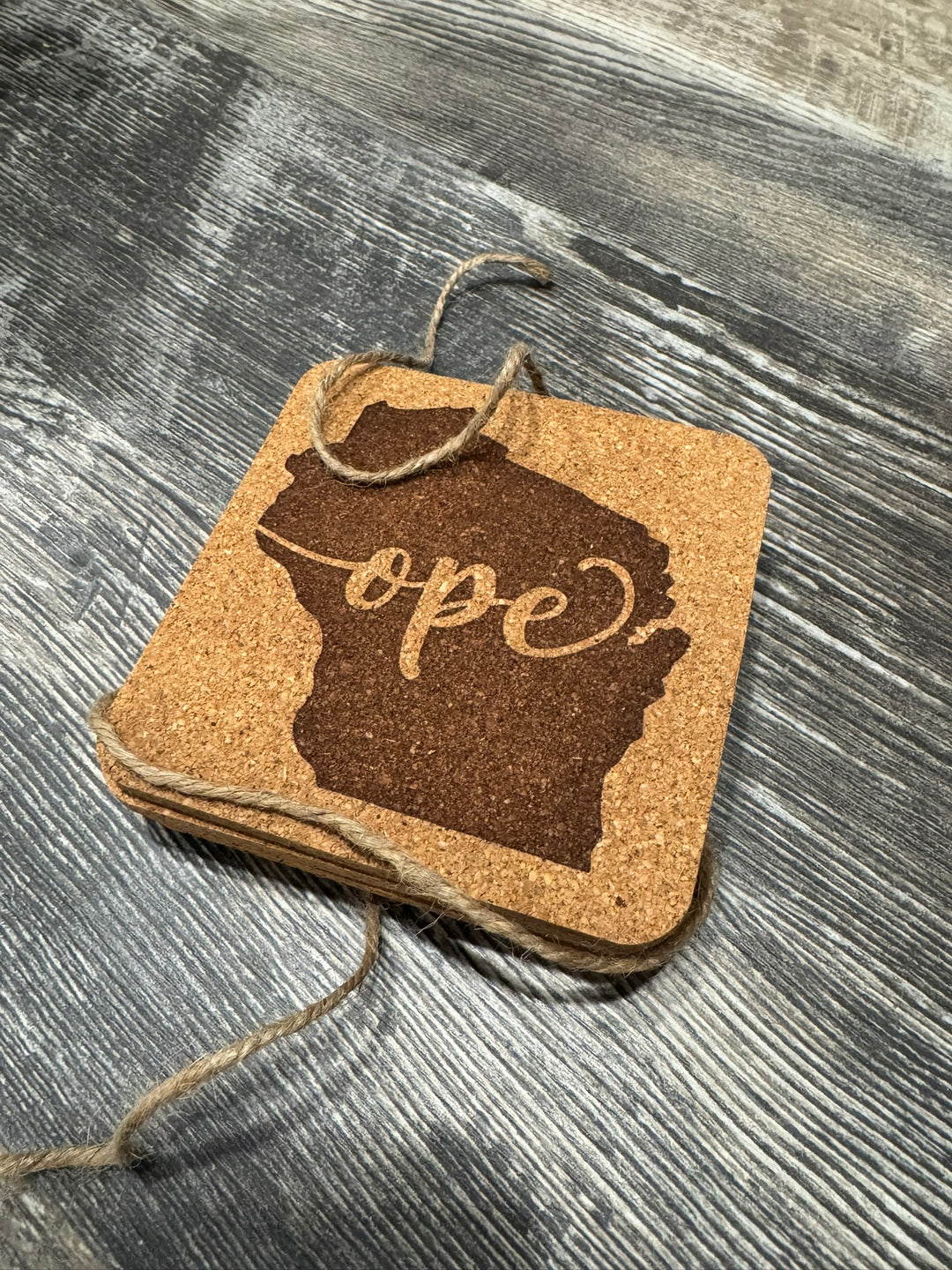 Cork coasters with the word "Ope" on a Wisconsin state silhouette. Brown twine to boot.