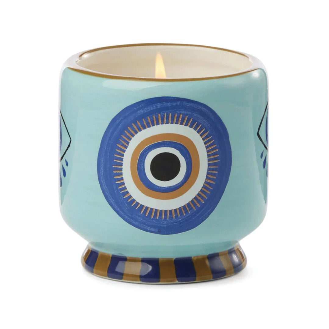 Footed ceramic vessel. Around the base are alternating squares of blue and brown. A gold line rims the top. In between is a stylized eye of blue and gold with a black iris.