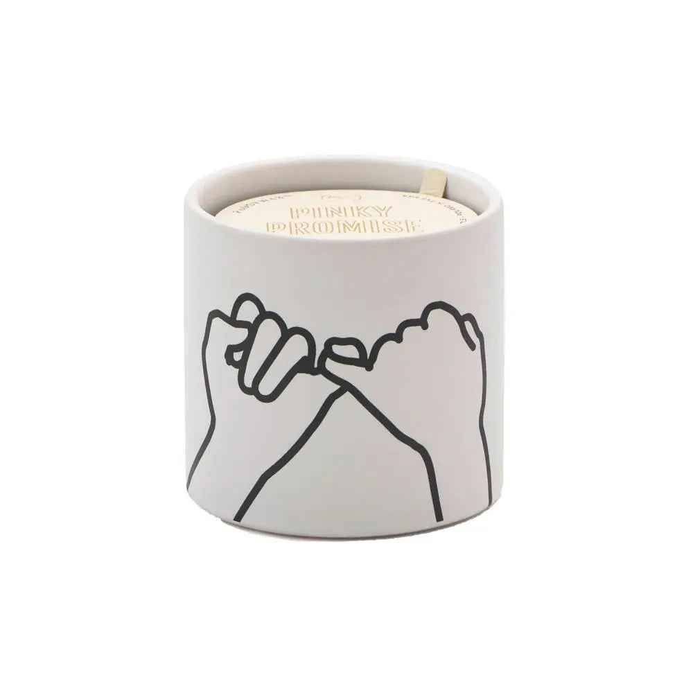 Scented candle in an off-white container with black line art showing two pinky fingers entwined. 