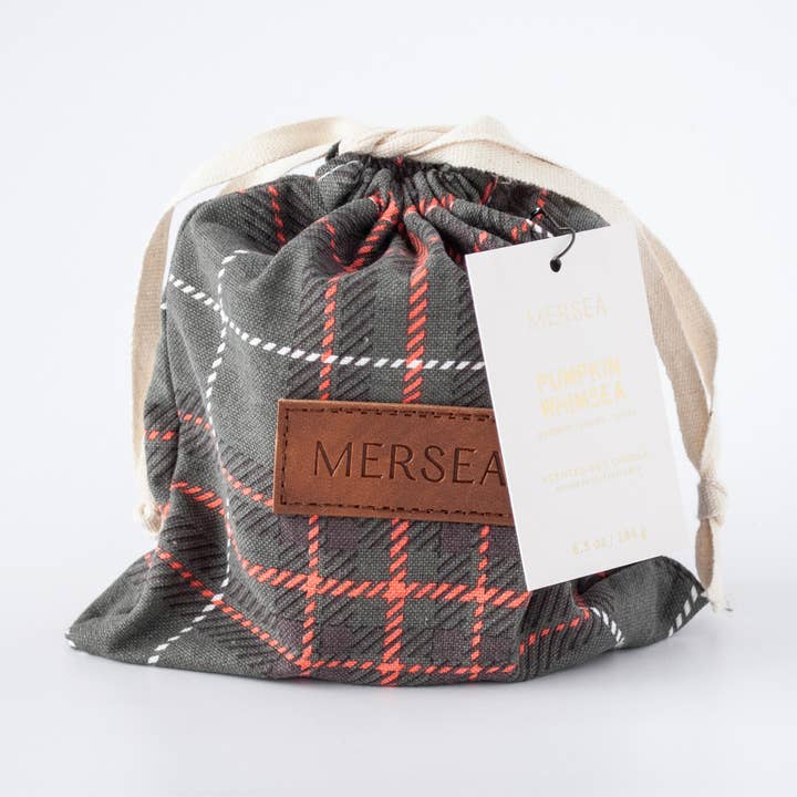 A gray, orange, and white plaid drawstring pouch with a brown leather patch embossed with 'MERSEA' and a gray hanging tag that reads 'MERSEA PUMPKIN WHIMSEA'.
