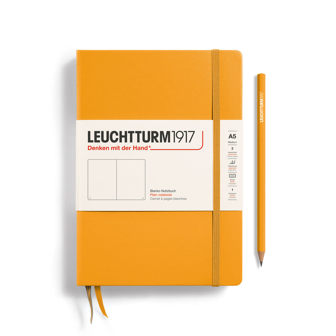 A Leuchtturm1917 A5 hardcover plain page notebook in rising sun orange with a white label on the front, shown closed with an elastic closure and ribbon bookmark. A matching rising sun orange pencil is placed vertically to the right.