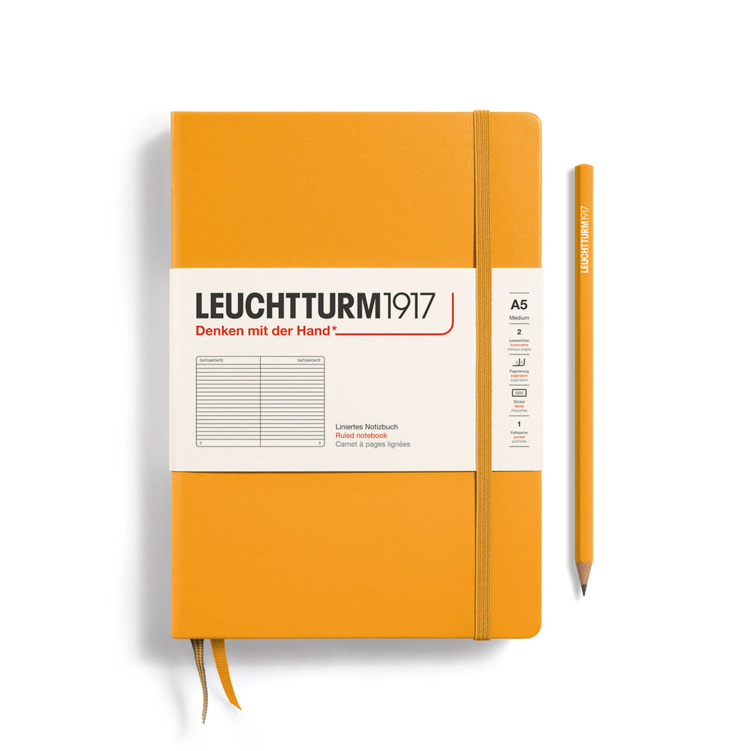 A Leuchtturm1917 A5 hardcover ruled page notebook in rising sun orange with a white label on the front, shown closed with an elastic closure and ribbon bookmark. A matching rising sun orange pensil is placed vertically to the right.