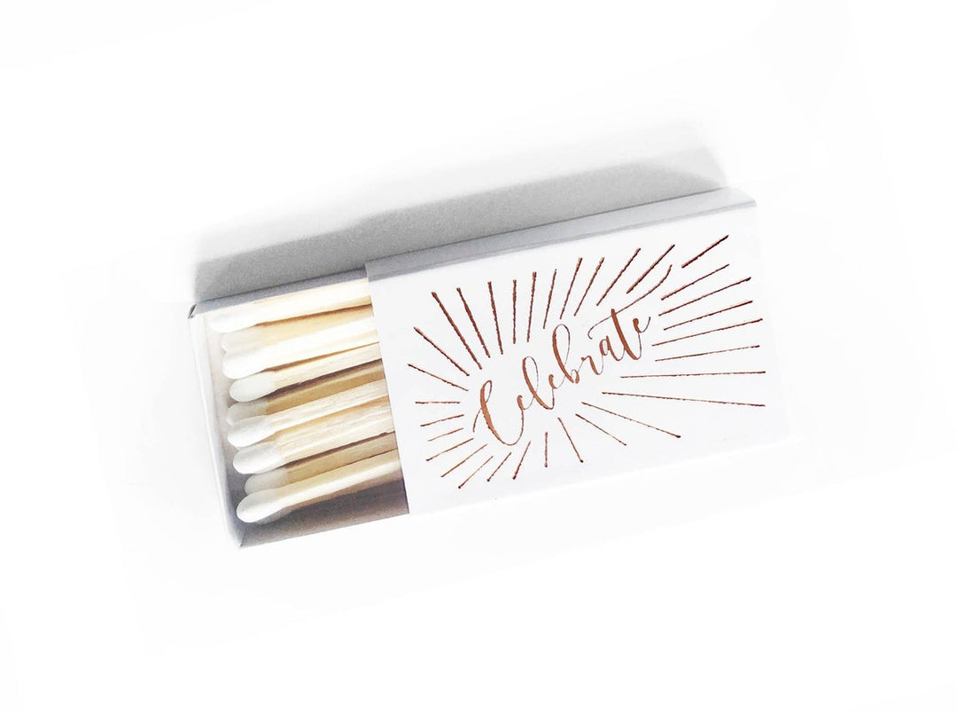 White matchbox with the word Celebrate in gold surrounded by a circle of fireworks- like lines.