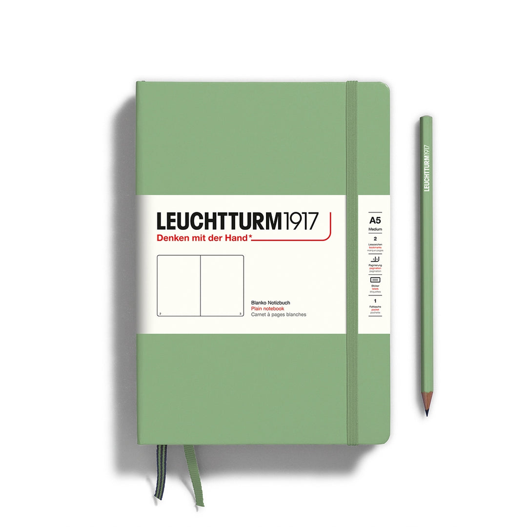 A Leuchtturm1917 A5 hardcover plain page notebook in sage green with a white label on the front, shown closed with an elastic closure and ribbon bookmark. A matching sage green pencil is placed vertically to the right.