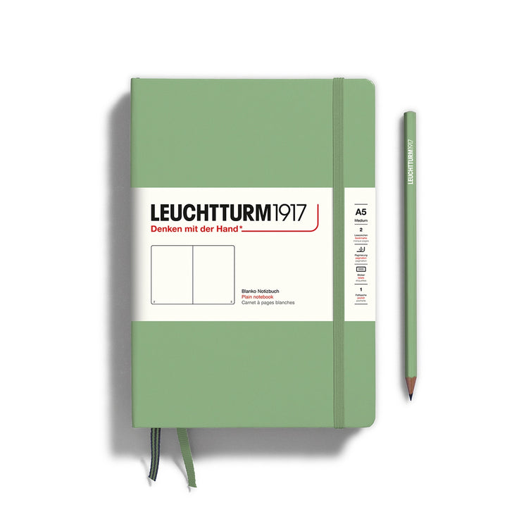 A Leuchtturm1917 A5 hardcover plain page notebook in sage green with a white label on the front, shown closed with an elastic closure and ribbon bookmark. A matching sage green pencil is placed vertically to the right.