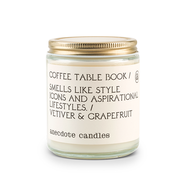 Coconut-soy wax candle in clear glass jar with lid. Label is Coffee Table Book/ Smells Like Style Icons and Aspirational Lifestyles / Vetiver & Grapefruit