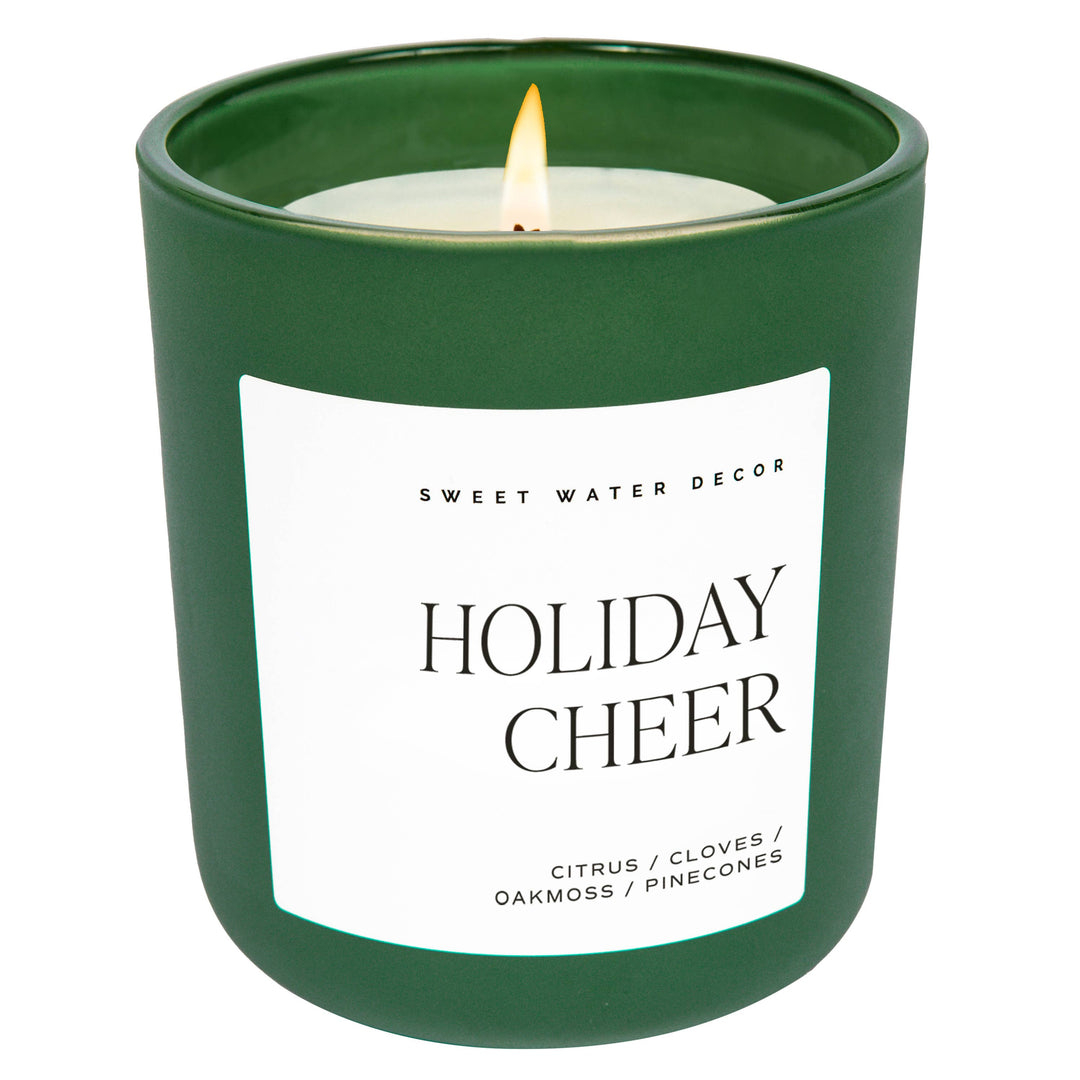 Scented soy candle in green matte glass container. Label is Holiday Cheer citrus / cloves / oakmoss / pinecones