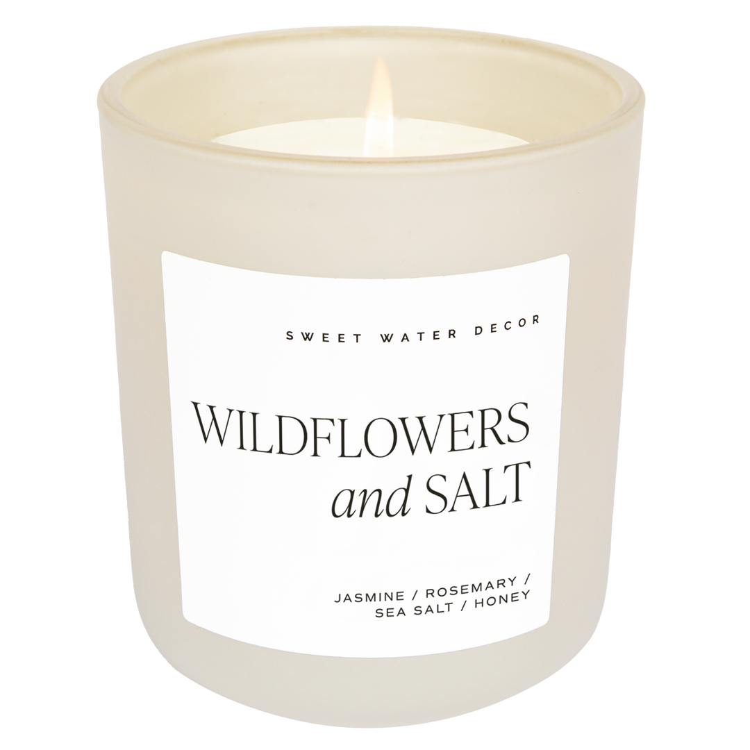 Scented soy candle in matte white glass container. Label is Wildflowers and Salt  Jasmine / Rosemary / Sea Salt / Honey