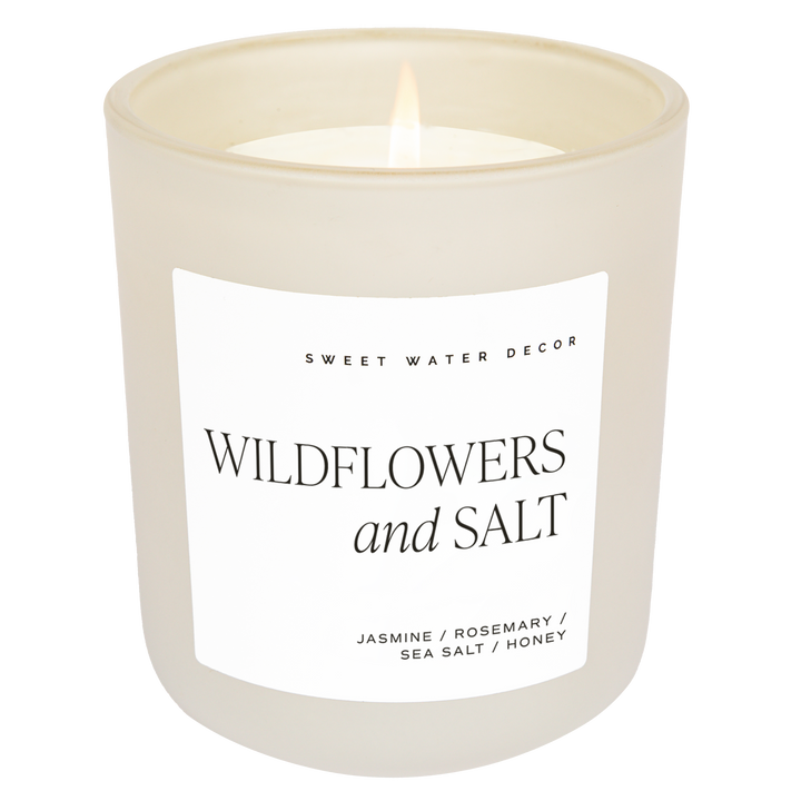 Scented soy candle in matte white glass container. Label is Wildflowers and Salt  Jasmine / Rosemary / Sea Salt / Honey