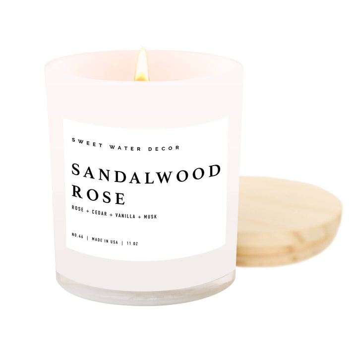 Lit candle in white opaque jar with b;acl text pm a white label and wooden lid.